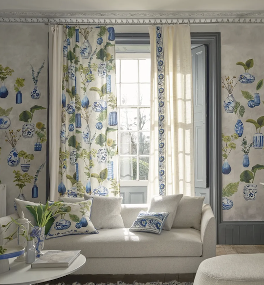 Woonkamer met gordijnen, kussens en behang uit de Designers Guild New Fabric Collectie 2025 met blauw-groene botanische prints.