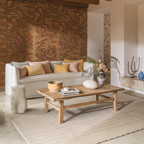Sfeervolle woonkamer met Élitis Tribu Samarkand behang, lichte bank met sierkussens, houten salontafel en natuurlijke materialen.
