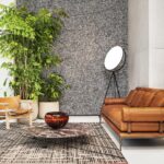 Modern ingerichte zithoek met een Lino Aspero wandbekleding, een leren bank, planten, designmeubels en een marmeren salontafel.