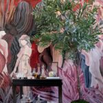Een kleurrijk interieur met een groene plant, glazen karaffen op een zwarte tafel en een wandbekleding met abstracte figuren uit de Arte collectie _97720_.