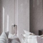 Sfeervol interieur met Arte Musa 75001 behang in een zacht bladmotief, gecombineerd met een moderne hanglamp en lichte kussens.