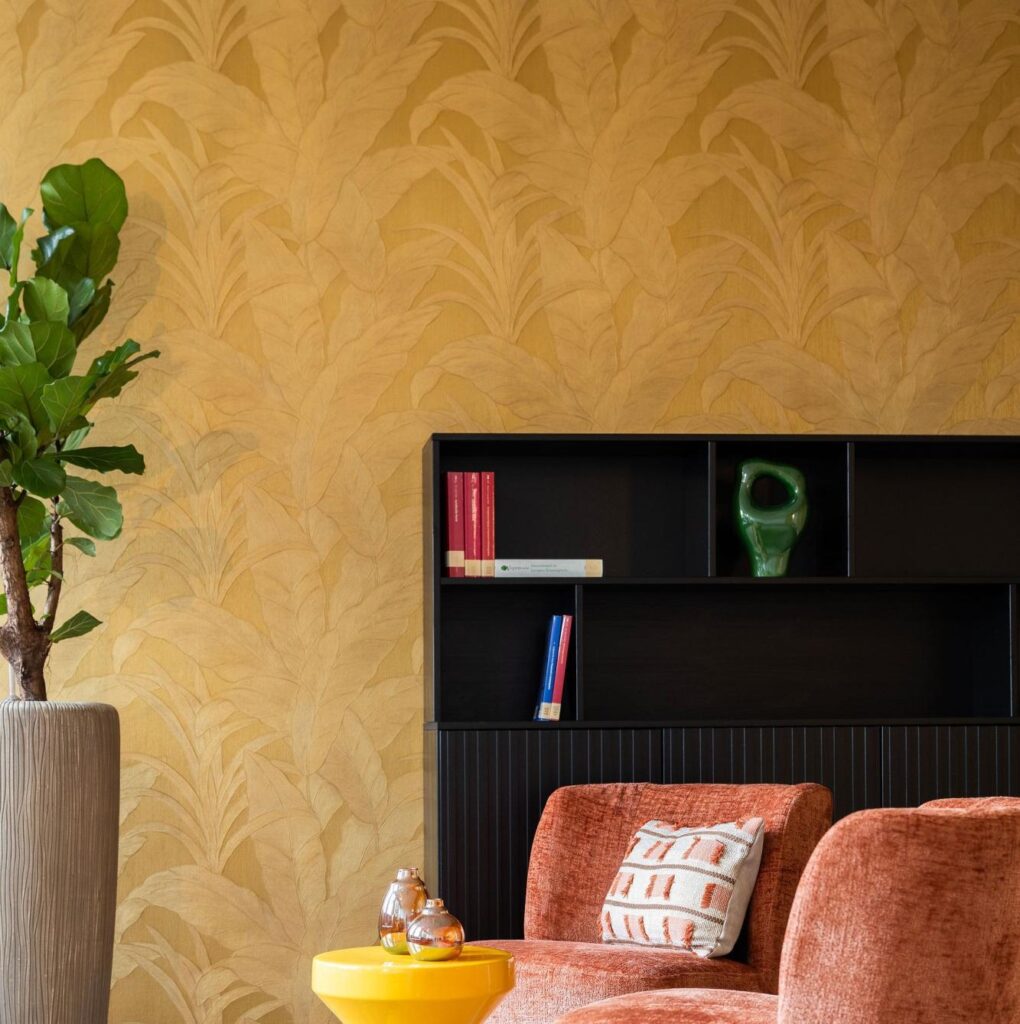 Sfeervol interieur met Arte Musa gold leaf behang, een fluwelen oranje fauteuil, een zwarte kast en groene kamerplant.
