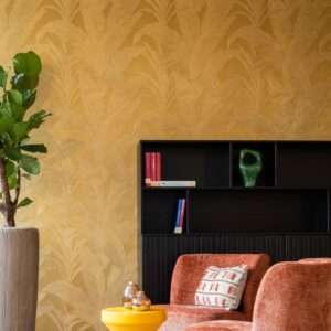 Sfeervol interieur met Arte Musa gold leaf behang, een fluwelen oranje fauteuil, een zwarte kast en groene kamerplant.