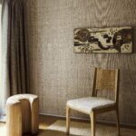 Sfeervolle interieurhoek met Arte Diffuse 52441 behang, een houten stoel, kunstwerk aan de muur en een organisch gevormd houten krukje.