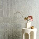 Minimalistisch interieur met Arte Diffuse 52443 behang, een witte vaas met sierlijke takken en roze-groene bladeren op een licht stenen tafeltje.