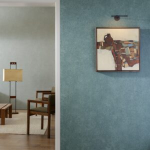 Moderne interieursetting met Arte Essentials Kaolin Calcaire Stucco behang in blauwgroene tint, een abstract schilderij en houten meubels.