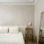 Sfeervol ingerichte slaapkamer met Arte Essentials Kaolin Fragment 30333 behang, een houten stoel en een hanglamp.