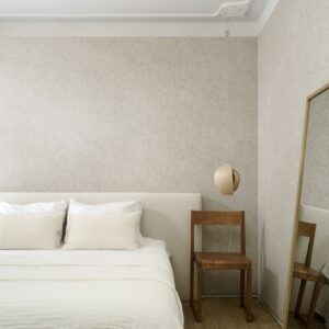 Sfeervol ingerichte slaapkamer met Arte Essentials Kaolin Fragment 30333 behang, een houten stoel en een hanglamp.