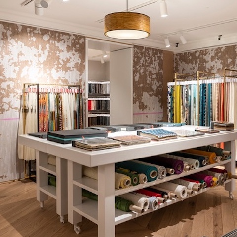 Showroom van ELITIS met een centraal werkblad en kleurrijke rollen stof en stalen langs de muren.