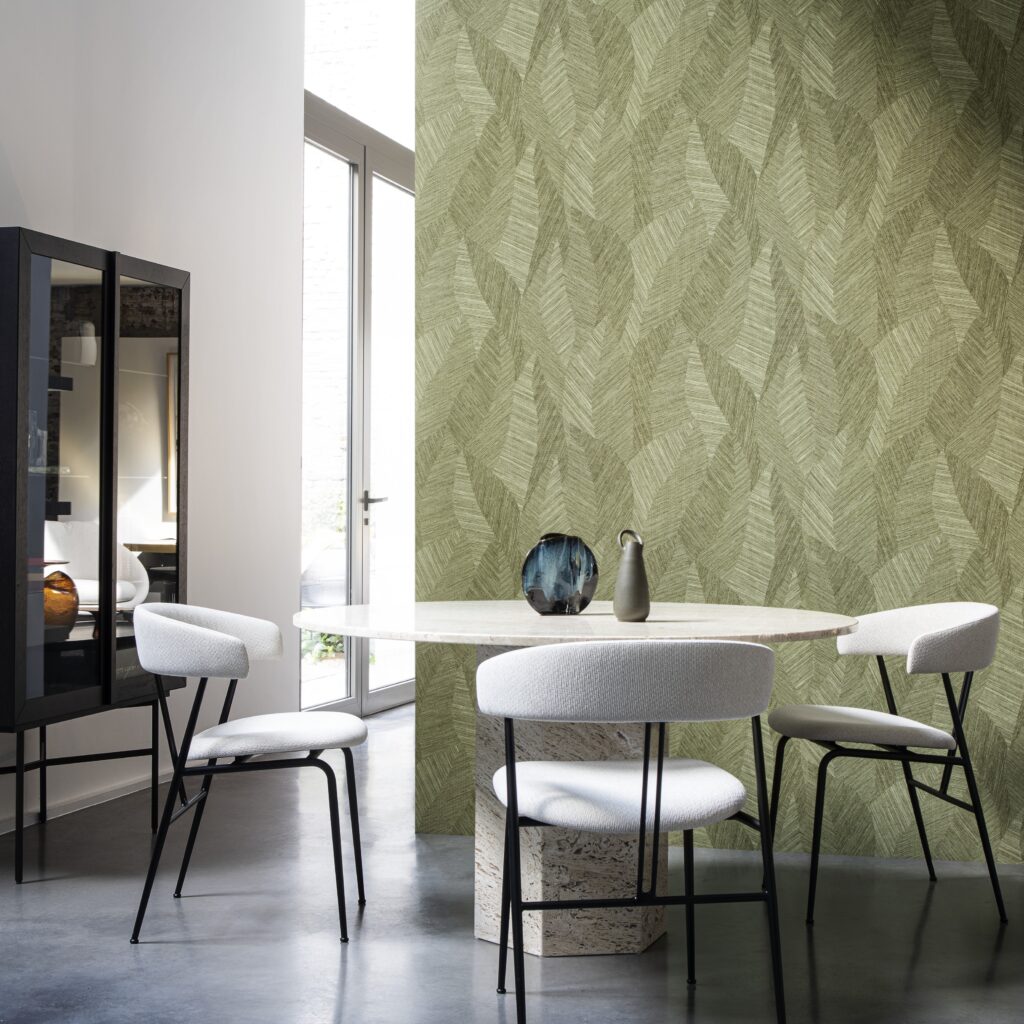 Moderne eetkamer met vier witte stoelen, een ronde tafel van natuursteen en een groene wand met het Tangram Bounty 24020 behang met bladpatroon.