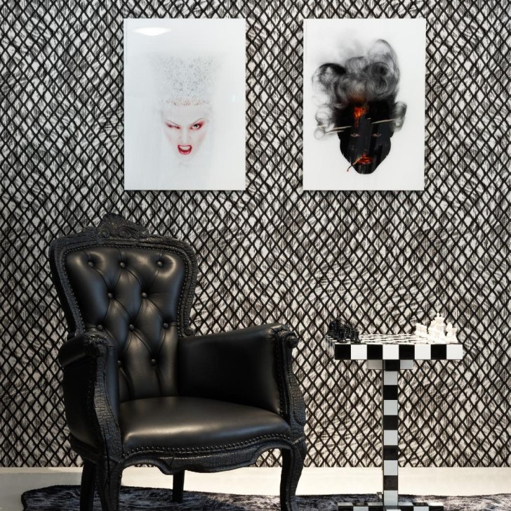 Zwartleren fauteuil naast schaaktafel met zwart-wit blokpatroon, voor een muur met artistieke portretten en grafisch behang.