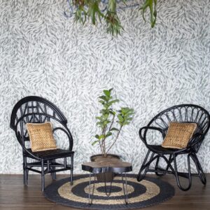 Twee zwarte rotanstoelen met gevlochten kussens staan op een rond vloerkleed voor een wand met Arte Moooi mo2041 behang, naast een kleine plant en organisch gevormd tafeltje.