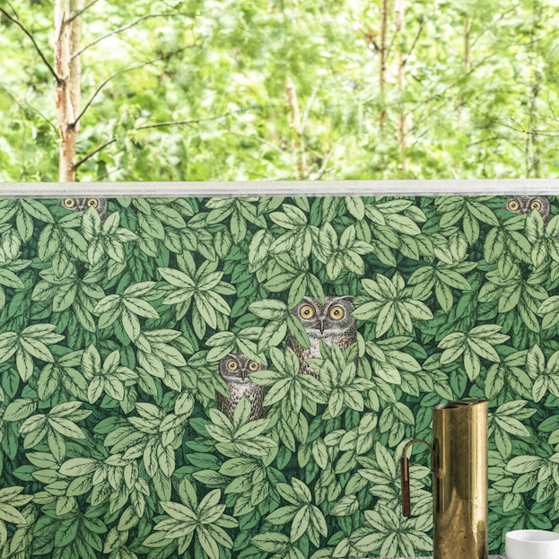 toepassing van het Fornasetti-behang Foglie e Civette met groene bladeren en tekeningen van uilen tussen het gebladerte.