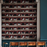 Toepassing op de muur van het Fornasetti-behang Theatro met elegante theaterbezoekers en rode gordijnen.