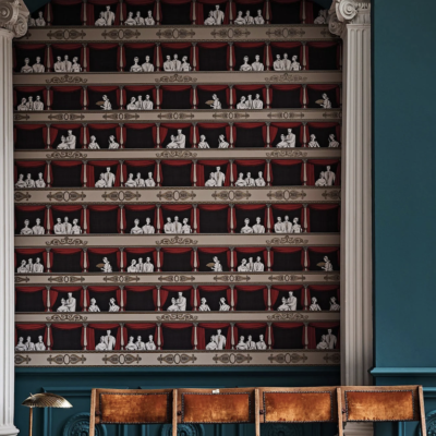 Toepassing op de muur van het Fornasetti-behang Theatro met elegante theaterbezoekers en rode gordijnen.