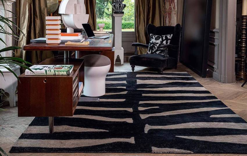Zwart-wit Elitis-vloerkleed Samburu met zebramotief in een werkkamer met houten bureau en zwarte fluwelen fauteuil.