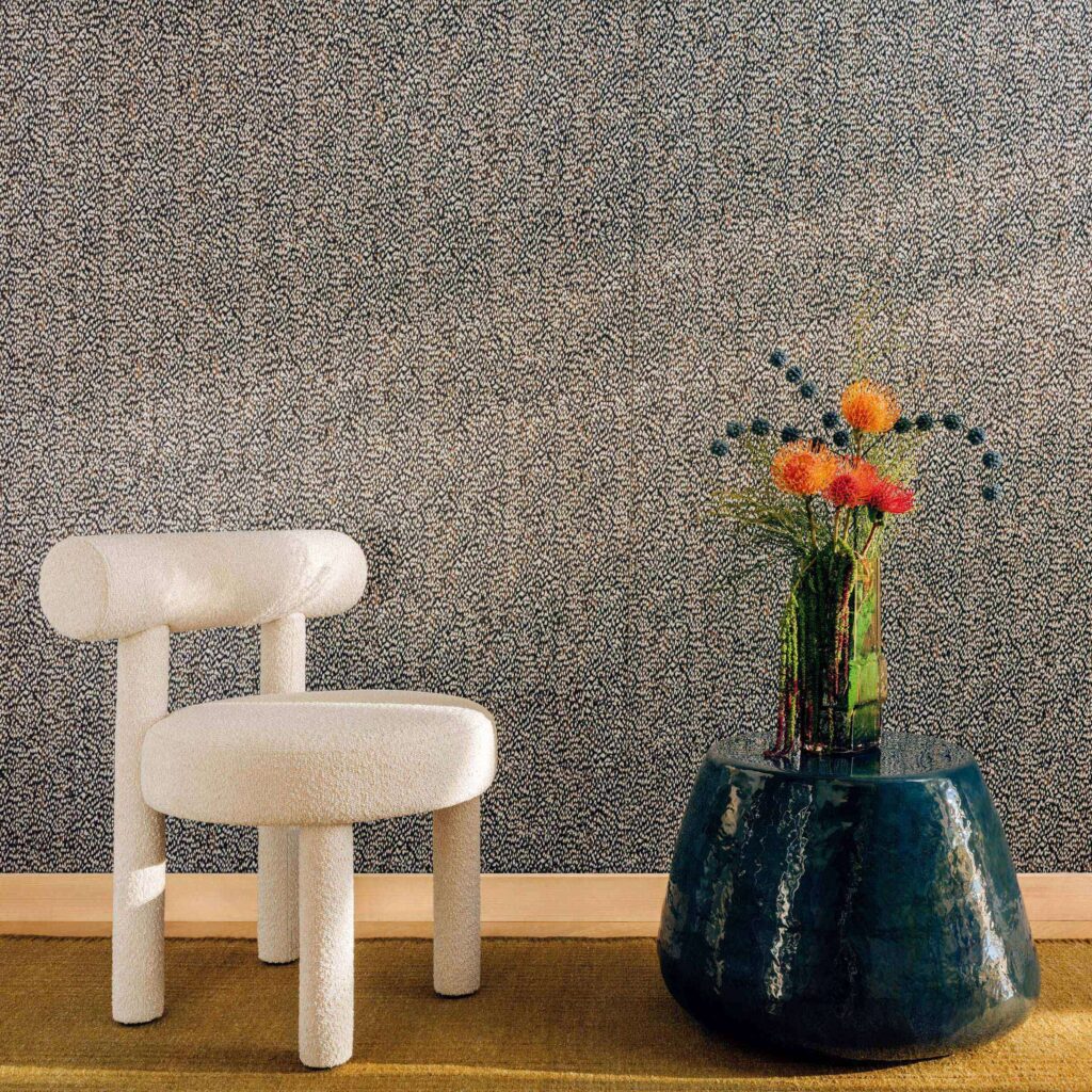 Elitis Cartagena Nuée RM 1148-80-behang met gespikkeld grijsblauw patroon, een witte bouclé stoel en blauwe bijzettafel.