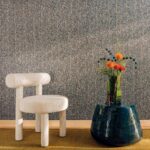 Elitis Cartagena Nuée RM 1148-80-behang met gespikkeld grijsblauw patroon, een witte bouclé stoel en blauwe bijzettafel.
