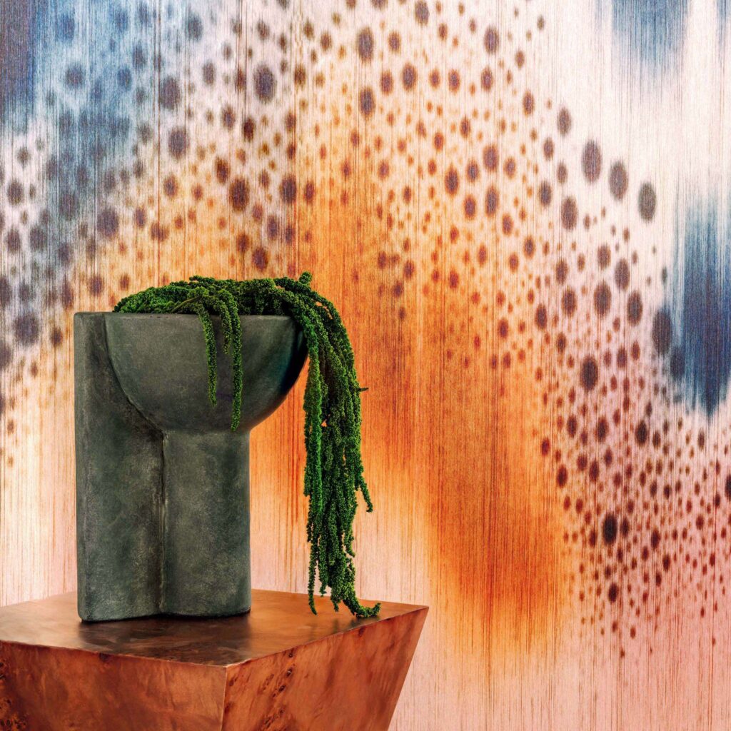 Elitis Cartagena Houle RM 1140-01-behang met stippen in oranje en blauw, achter een stenen vaas met hangplant.